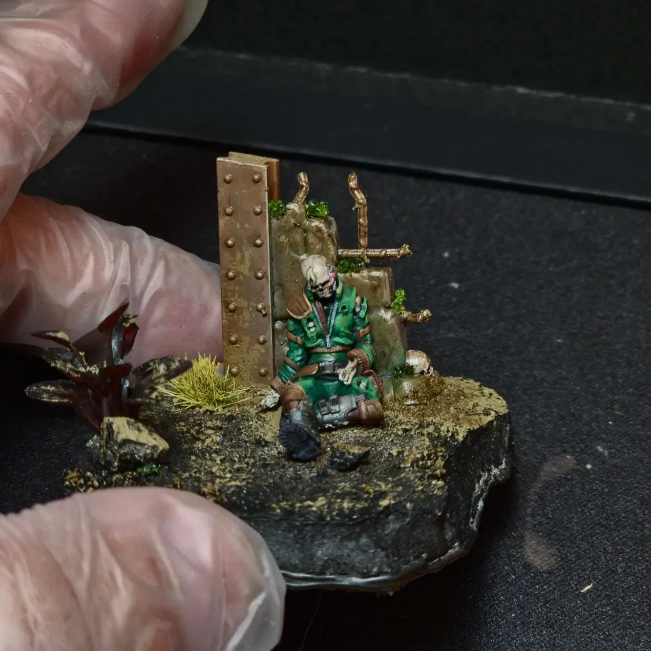 Diorama med ett skelett i grön uniform som sitter mot en rostig vägg
